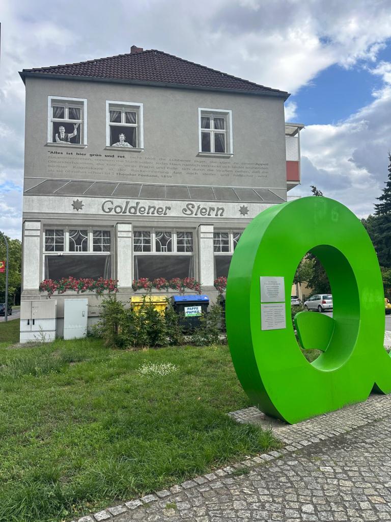 Großer Buchstabe Q vor einem grauen Gebäude auf dem "Goldener Stern" steht
